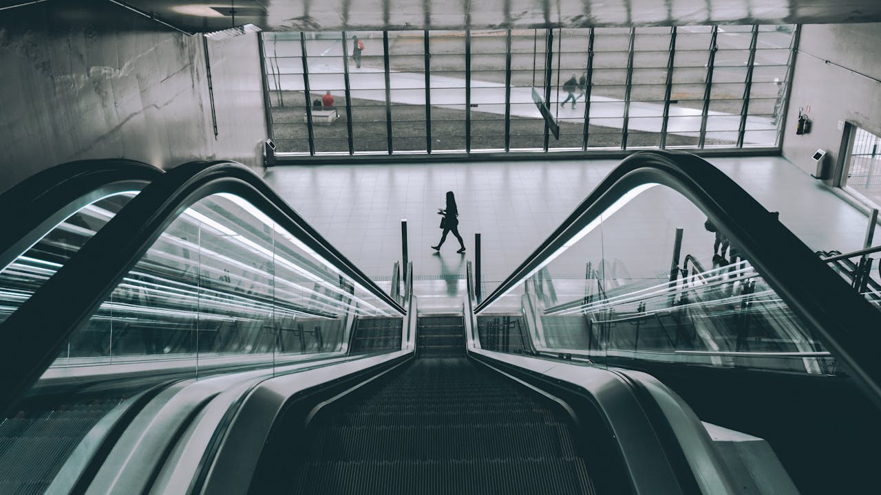 People using the sleek modern escalator in an indoor building with glass panels.